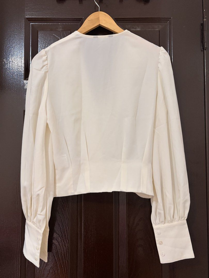 ASM ANNA White Long Sleeve V-Neck Blouse (Category: Longsleeves) located in Marikina City. Submitted by _bananahanaa (Listing ID 1470768381, Image 2). Description: - Brand/Style: ASM ANNA white blouse - Design: Deep V-neck, long bishop sleeves with 3-button cuffs, and front/back pleats - Fit: Cropped style - Flaws: Has a few light yellowish stains near the right shoulder area (see last photo for reference).