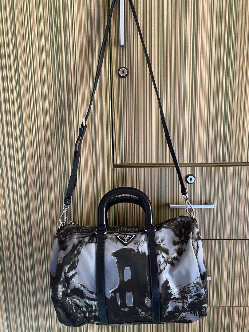 Authentic Prada Landscape Print Nylon Duffle Handbag (Category: Luxury Bags & Wallets) located in Taguig. Submitted by sandzclick (Listing ID 1470766495, Image 2). Description: - Authentic Prada nylon duffle bag in a chic black and grey landscape print - Dual rolled leather top handles and detachable black leather shoulder strap - Silver-tone hardware with metal protective feet on the base - Iconic Prada enamel triangle logo on the front - Secure