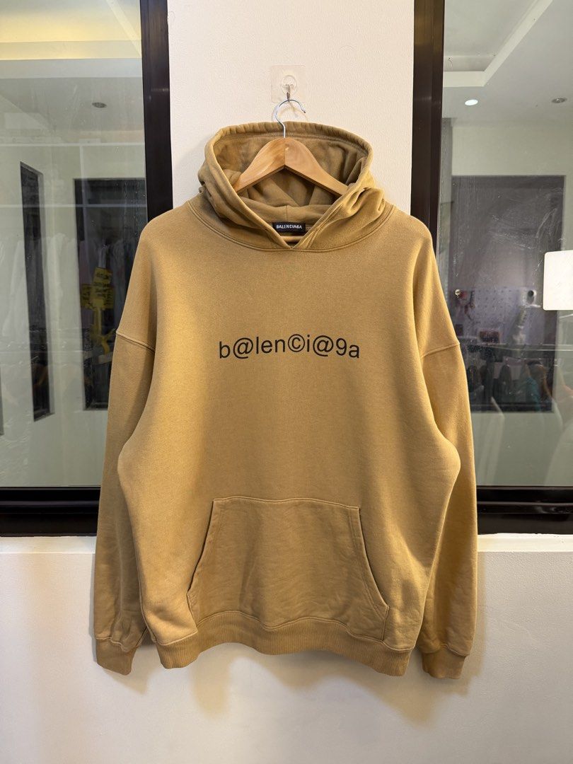 Balenciaga Pullover Hooded Sweatshirt (Category: Coats, Jackets and Outerwear) located in Paranaque City. Submitted by preluxeshop_ph (Listing ID 1470816809, Image 2). Description: Brand: Balenciaga •Style: Pullover Hooded Sweatshirt / Hoodie •Color: Camel / Desert Tan •Design Features: Black “b@lencỉ@g@“-style graphic text across the chest, attached hood, and front kangaroo pocket •Made In: Portugal •Condition: Pre-loved / Excellent condition.