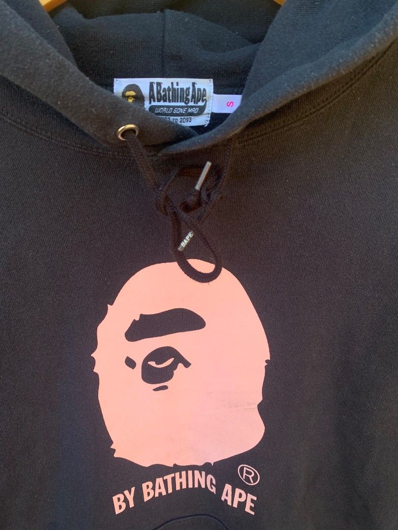 BAPE Pink Ape Head Ladies (Category: Coats, Jackets and Outerwear) located in Aloran. Submitted by chester78864 (Listing ID 1470931181, Image 2). Description: - Brand: A Bathing Ape (BAPE) - Item: Black Hoodie - Size: Small - Design: Large pink ape head graphic with "By Bathing Ape" text on the chest - Features: Kangaroo pocket, drawstrings with branded metal aglets - Details: Includes original interior neck tags and wash tags showing product cod