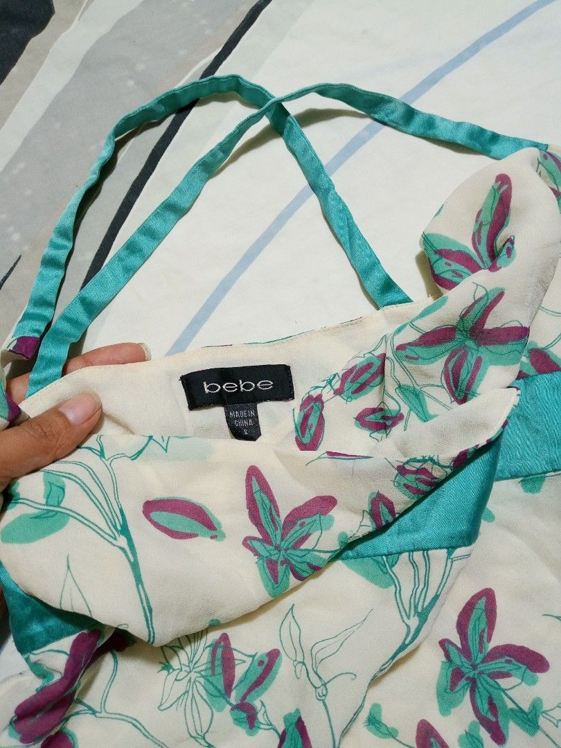 bebe Floral Halter Tank Top Size S (Category: Sleeveless) located in Dumaguete. Submitted by morie_luna15 (Listing ID 1470839676, Image 2). Description: - Brand: Bebe - Style: Y2K halter tank top with a layered hem - Color/Print: Cream with green and purple floral print - Details: Teal satin band under the bust - Size: S (tag on collar) - Material: Lightweight fabric - Origin: Made in China - Condition: Great pre-loved piece.
