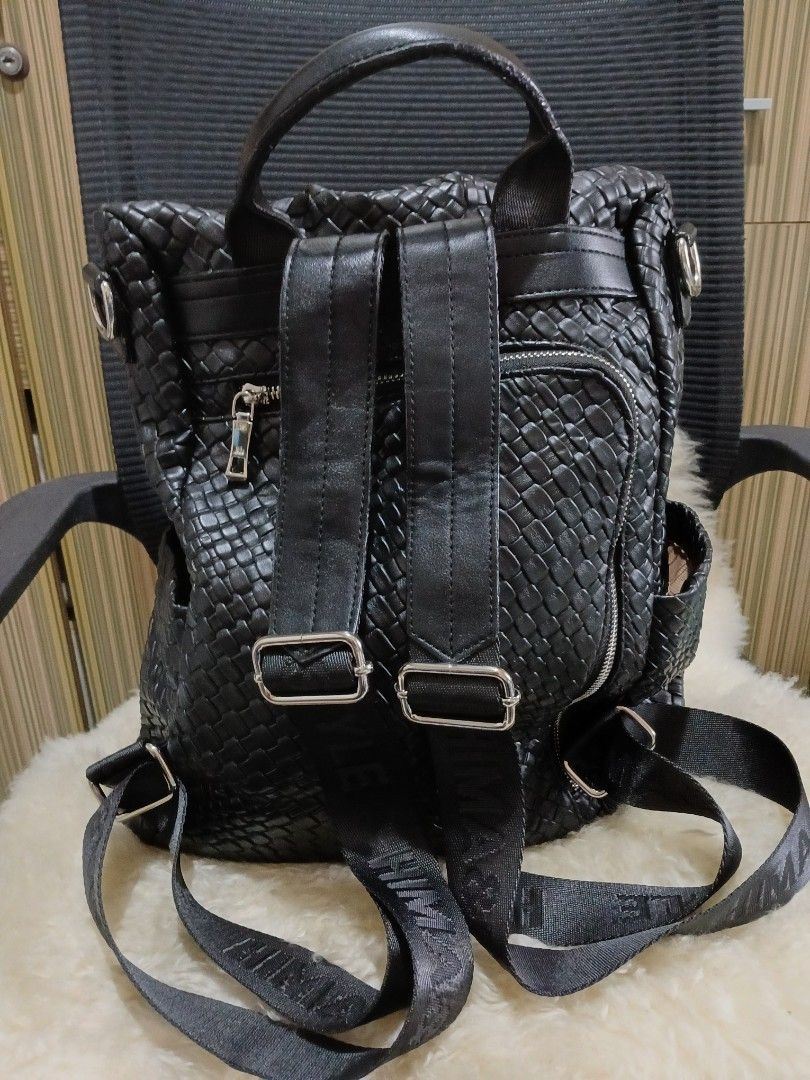Black Woven Leather Backpack with Branded Straps (Category: Backpacks) located in Taguig. Submitted by demsclosetph (Listing ID 1470795149, Image 2). Description: - Color/Material: Black woven faux leather - Hardware: Silver-tone with crystal-accented round front logo plate - Straps: Adjustable fabric straps with stylish printed lettering - Pockets: Secure zippered main compartment and exterior zip pocket - Convenience: Top grab handle included -