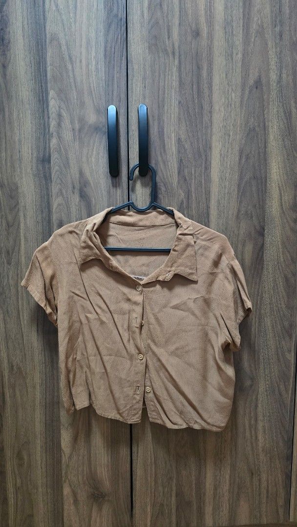 Brown short sleeve button up collared cropped shirt (Category: Shirts) located in Manila. Submitted by stuff.gaming (Listing ID 1470807048, Image 1). Description: - Color: Brown - Cut: Cropped with classic collar - Sleeves: Short sleeves - Details: Light brown front buttons, plain back with yoke seam - Material: Soft textured fabric - Condition: Clean and ready to wear - Styling: Perfect to pair with high-waisted jeans or skirts Price still negot
