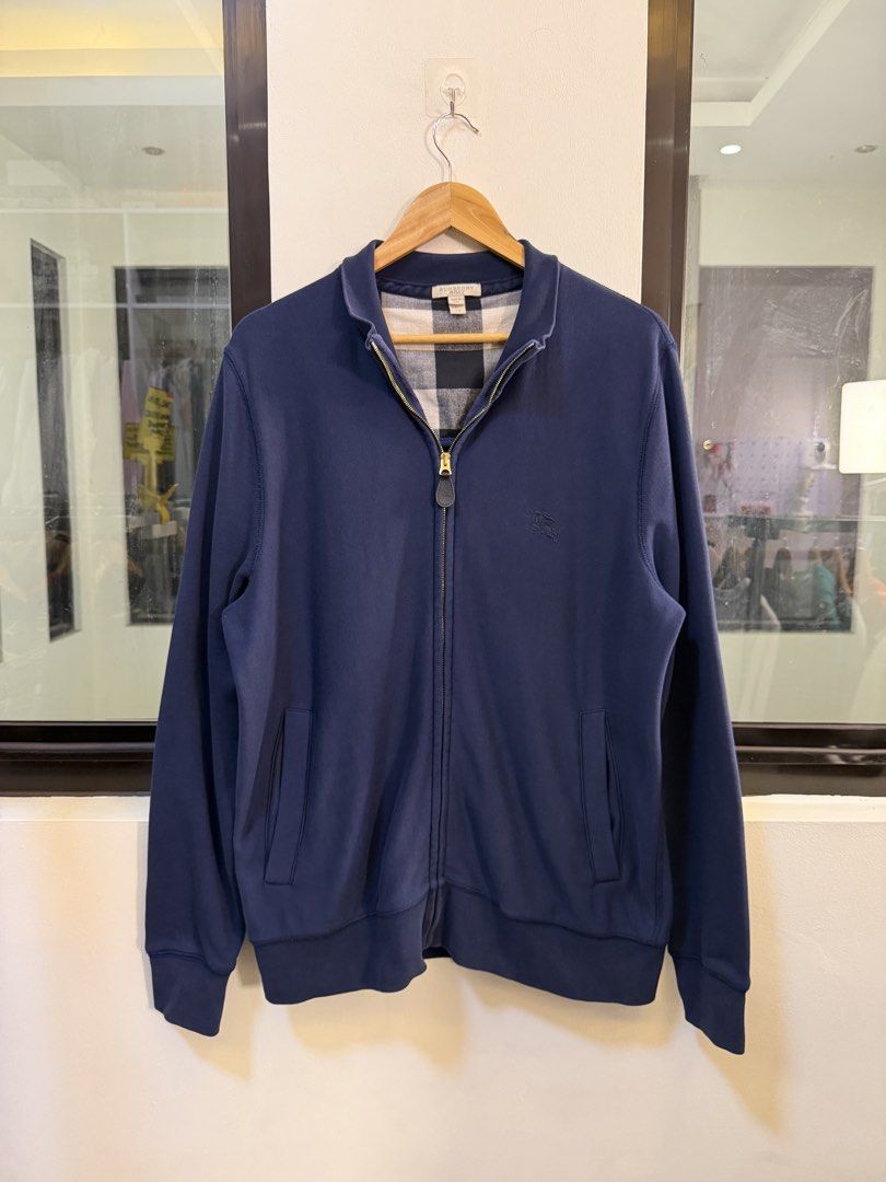 Burberry Full-Zip Track Jacket (Category: Coats, Jackets and Outerwear) located in Paranaque City. Submitted by preluxeshop_ph (Listing ID 1470817692, Image 2). Description: Brand: Burberry Brit •Style: Full-Zip Track Jacket / Sweatshirt •Color: Dark Navy Blue •Design Features: Full front zip closure with gold-tone hardware, stand-up collar, front welt pockets, ribbed cuffs and hem, and signature plaid check inner lining •Tag Size: Extra Large (X