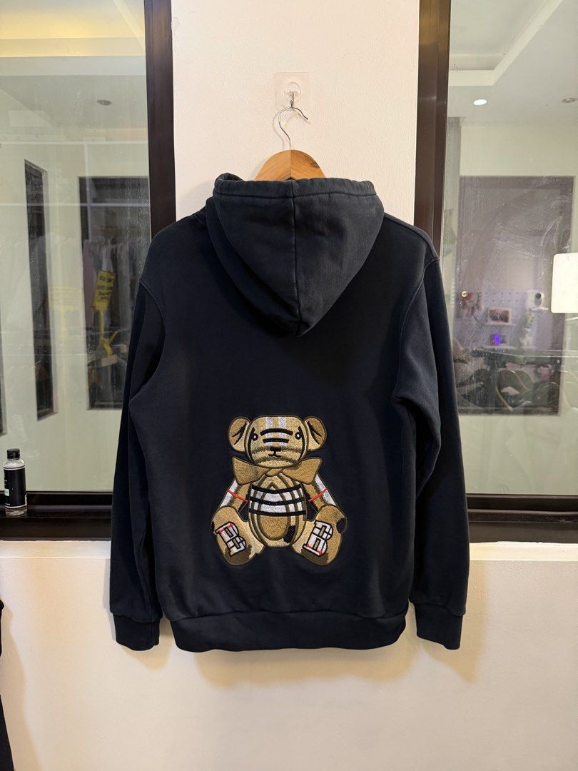Burberry Pullover Hoodie (Category: Coats, Jackets and Outerwear) located in Paranaque City. Submitted by preluxeshop_ph (Listing ID 1470813527, Image 3). Description: Brand: Burberry London England -Style: Pullover Hoodie / Hooded Sweatshirt -Color: Dark Navy Blue -Design Features: Printed white Burberry London England logo across the chest, Thomas Bear motif graphic patch on the back, drawstring hood, and front kangaroo pocket -Material Composi