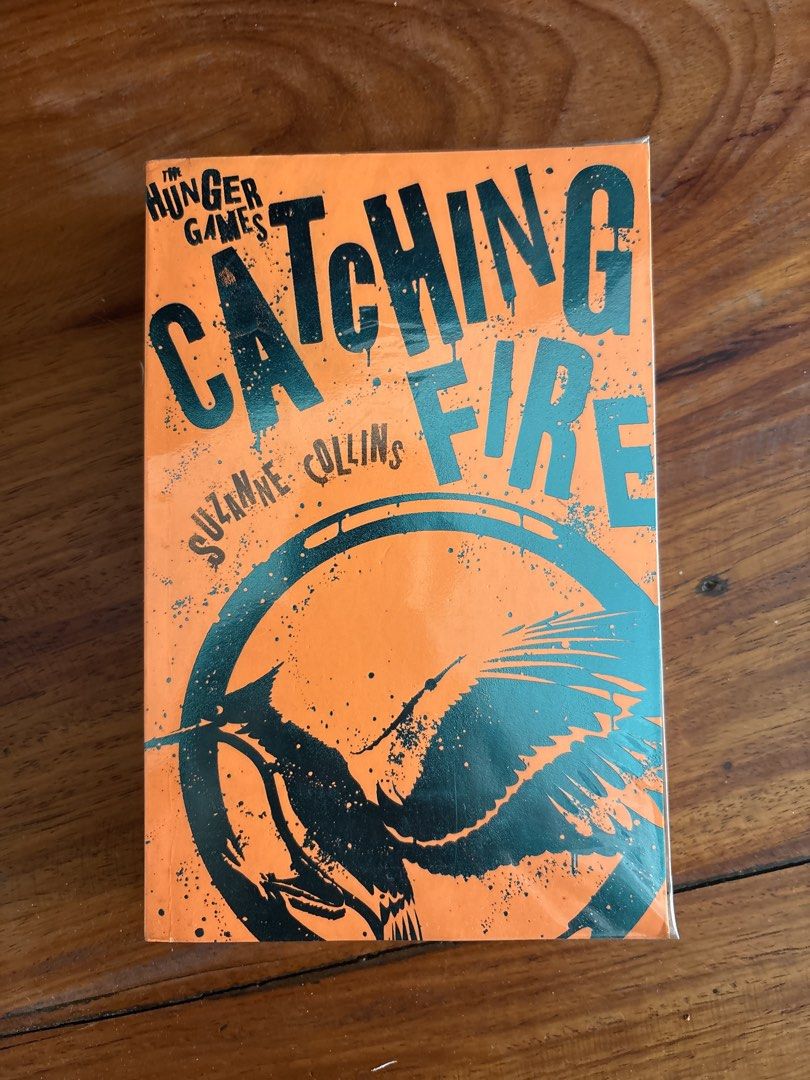 Catching Fire by Suzanne Collins The Hunger Games (Category: Storybooks) located in Makati City. Submitted by garagesllr007 (Listing ID 1470750477, Image 1). Description: - Title: Catching Fire (The Hunger Games Series #2) - Author: Suzanne Collins - Format: Paperback with bright orange cover and black mockingjay emblem - Extra: Fully covered in clear protective plastic wrap - Genre: Dystopian fiction.
