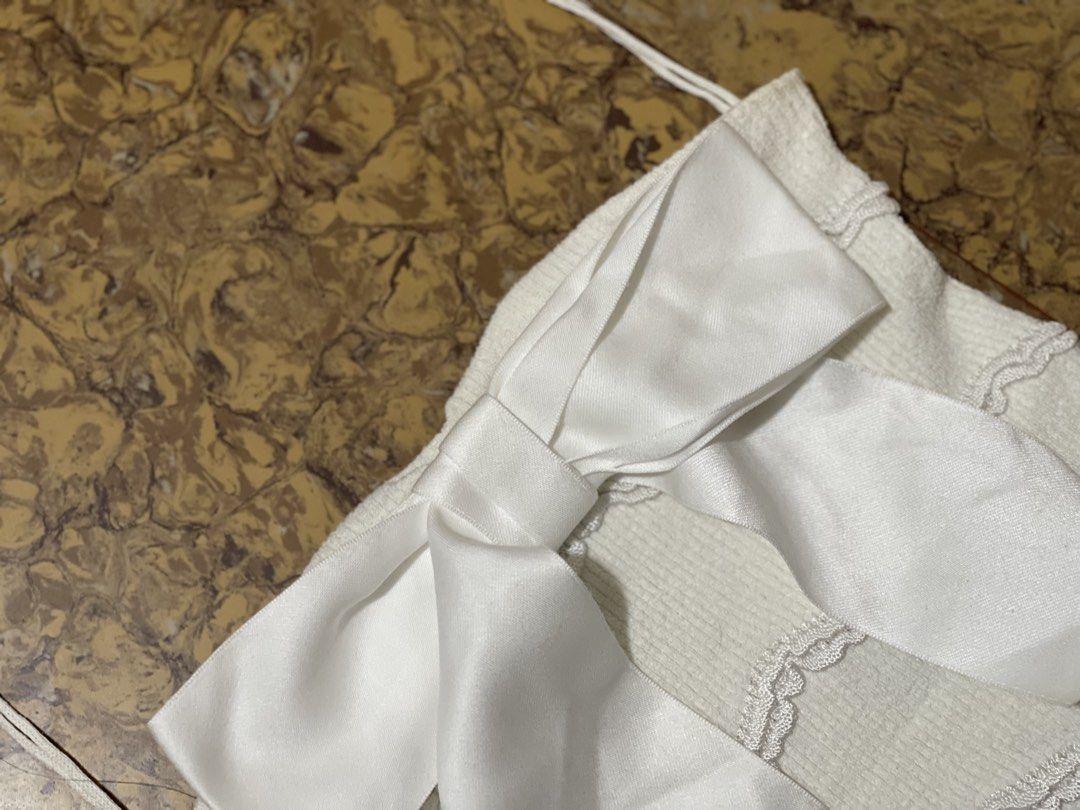 Chanel white cotton knit top (Category: Luxury Apparel) located in Marikina City. Submitted by joshuaades21107 (Listing ID 1470865020, Image 2). Description: Chanel white cotton knit top featuring a prominent satin bow and a small metal CC logo charm (style/reference code P70342 / P70342K10011, size 36) White knit sleeveless/strap top with wavy/ribbed pattern details, a large white satin bow on the front, and a CC logo emblem at the bottom corner