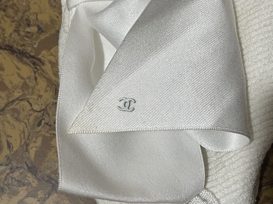 Chanel white cotton knit top (Category: Luxury Apparel) located in Marikina City. Submitted by joshuaades21107 (Listing ID 1470865020, Image 3). Description: Chanel white cotton knit top featuring a prominent satin bow and a small metal CC logo charm (style/reference code P70342 / P70342K10011, size 36) White knit sleeveless/strap top with wavy/ribbed pattern details, a large white satin bow on the front, and a CC logo emblem at the bottom corner