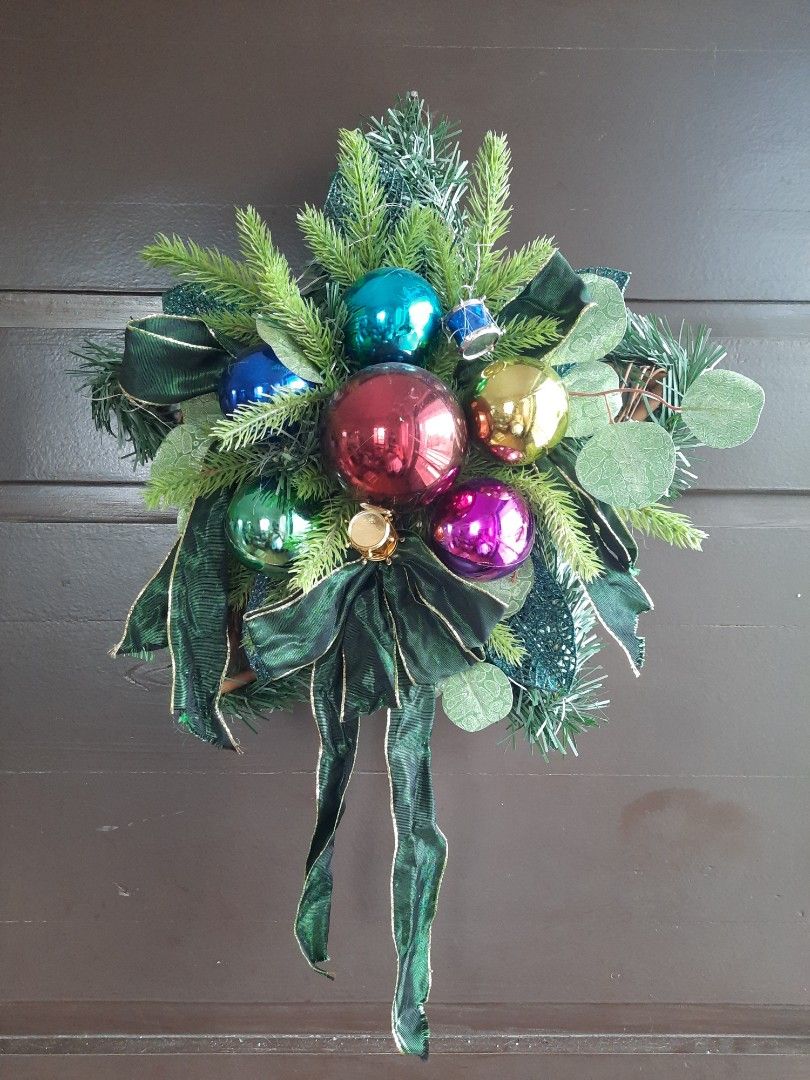 Christmas Wreath/Swag (Category: Wall Decor) located in Marilao. Submitted by mariealeiah (Listing ID 1470756147, Image 1). Description: - Festive holiday wreath/swag for front doors or walls - Decorated with colourful shiny baubles (red, gold, purple, blue, green) - Lush green pine branches mixed with eucalyptus leaves - Features a dark green velvet-style ribbon bow with gold trimming - Ready to hang for the Christmas season.