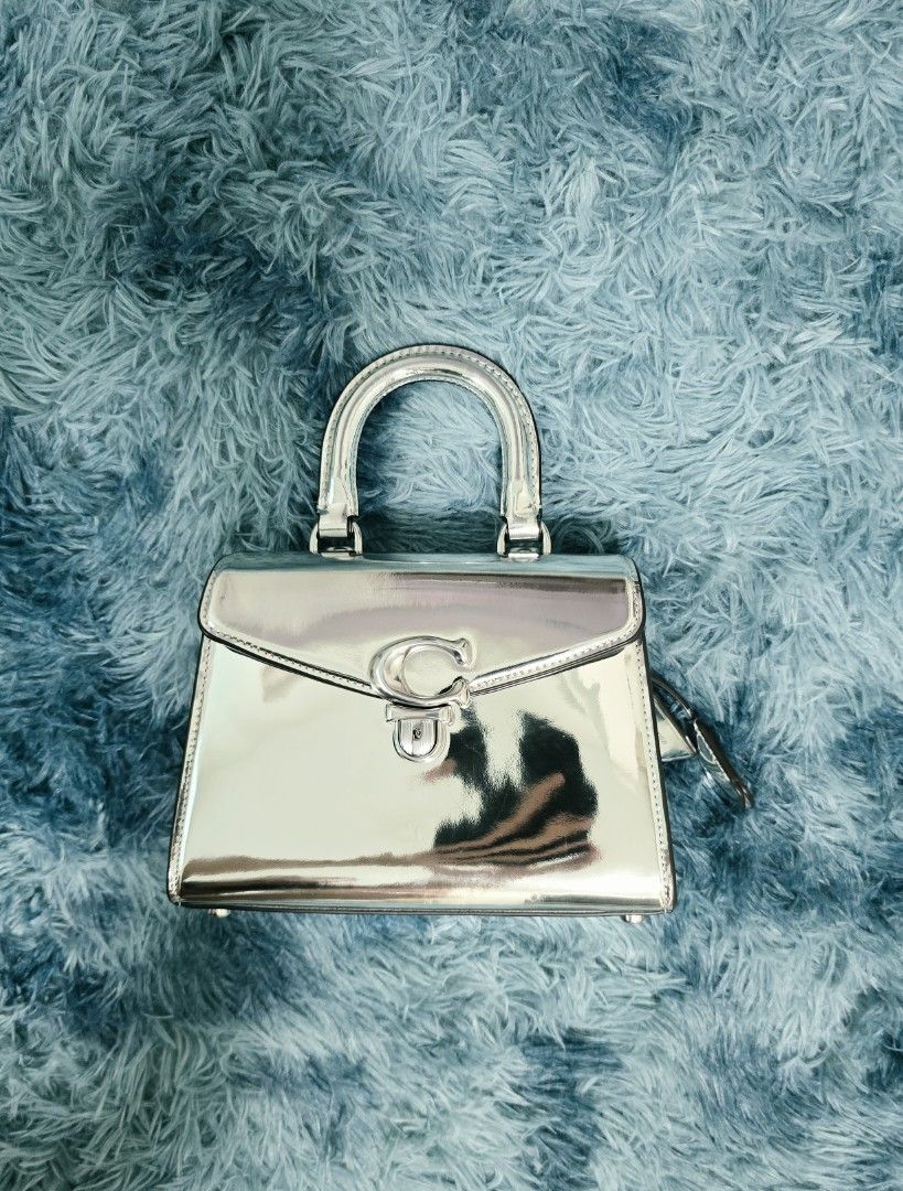 Coach Metallic Silver Top Handle Handbag (Category: Shoulder Bags) located in Bacolod City. Submitted by herclosetjoy (Listing ID 1470754297, Image 1). Description: - Authentic Coach metallic silver handbag - Structured shape with a trendy glossy mirror finish - Iconic metal 'C' twist lock front flap closure - Convenient single top handle with sturdy metal hardware - Compact size with clean lines and well-maintained bottom corners.
