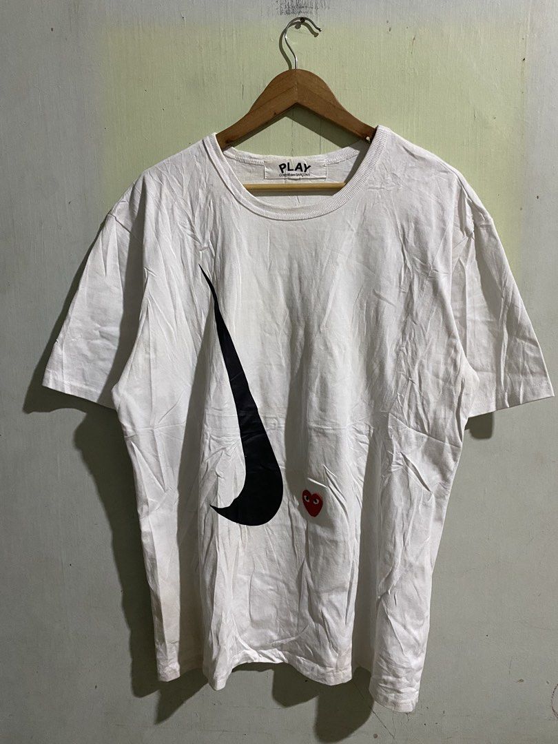 COMME des GARÇONS PLAY x Nike White Tee (Category: Shirts) located in Pandi. Submitted by nasya_thrift_collection2023 (Listing ID 1470858023, Image 1). Description: - Brand: PLAY COMME des GARÇONS x Nike - Color: White with black swoosh and red heart prints - Material: 100% Cotton, Made in Japan - Model: AZ-T026 (AD2020 collection) - Condition: Normal wear, clean fabric, crisp prints .