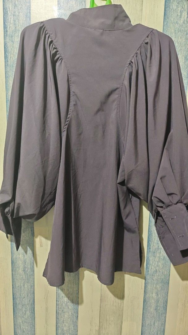 Dark Grey High Neck Long Sleeve Blouse with Statement Sleeves (Category: Longsleeves) located in Quezon City. Submitted by miladyie (Listing ID 1470858562, Image 2). Description: - Color: Dark Grey - Sleeves: Dramatic bishop sleeves with fitted cuffs - Neckline: High collar with front button closure - Design: Unique front and back seaming details with side slits at the hem - Fabric: Smooth material with a subtle sheen - Fit: Relaxed and stylish S