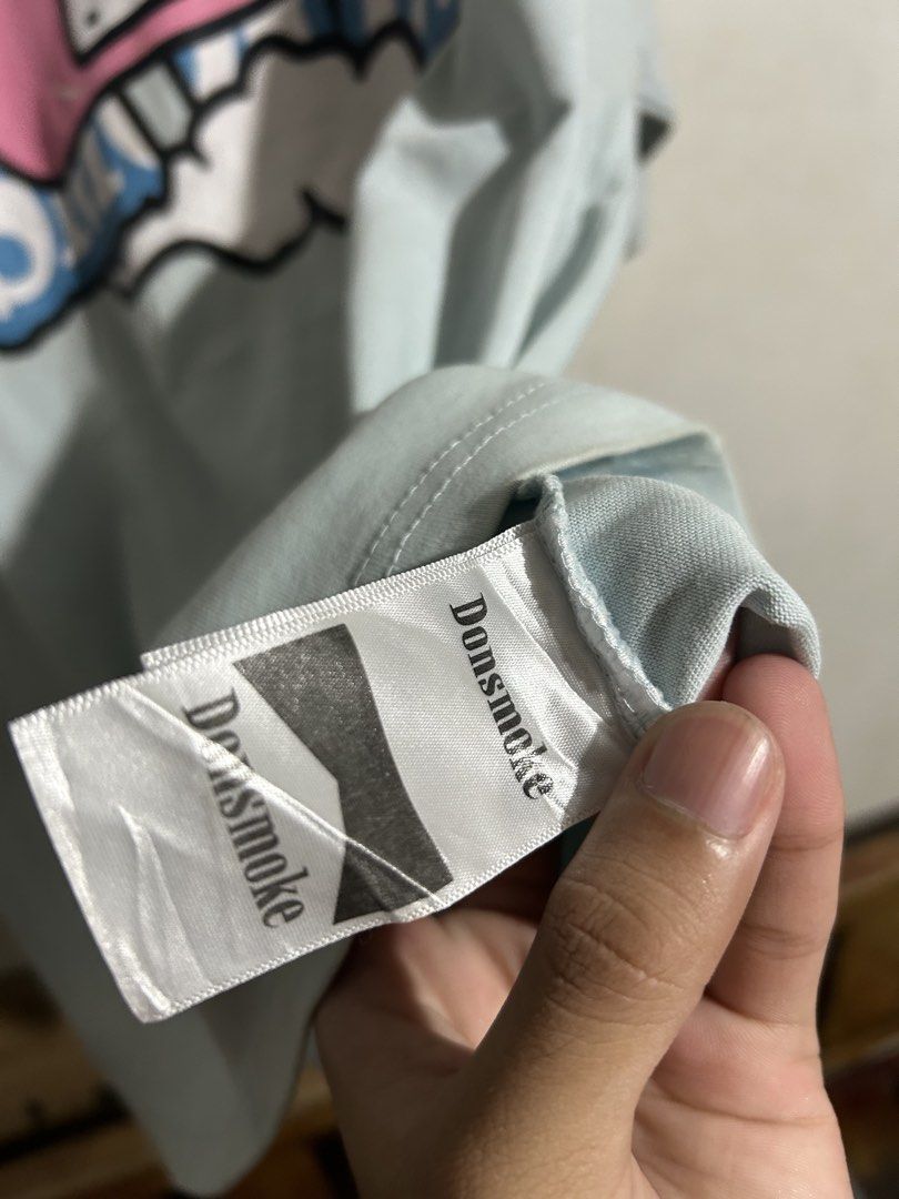 Donsmoke Graphic Tee Light Blue Size L (Category: Tshirts & Polo Shirts ) located in Manila. Submitted by romnick907 (Listing ID 1470819320, Image 3). Description: - Brand: Donsmoke - Color: Light Blue - Size: Large (tag at collar and inner hem) - Design: Large front graphic featuring a crown, cloud, and pink adhesive bandage motif - Material: Clean, high-quality cotton with vibrant screen-print - Condition: Excellent/Ready to wear.