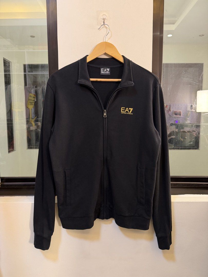 Emporio Armani Full-Zip Track Jacket (Category: Coats, Jackets and Outerwear) located in Paranaque City. Submitted by preluxeshop_ph (Listing ID 1470812638, Image 2). Description: Brand: EA7 Emporio Armani -Style: Full-Zip Track Jacket / Stand-Collar Sweatshirt -Color: Black with gold-tone accents -Design Features: Gold EA7 Emporio Armani logo on the left chest, gold signature vertical line graphic on the upper back collar, full front zip closure
