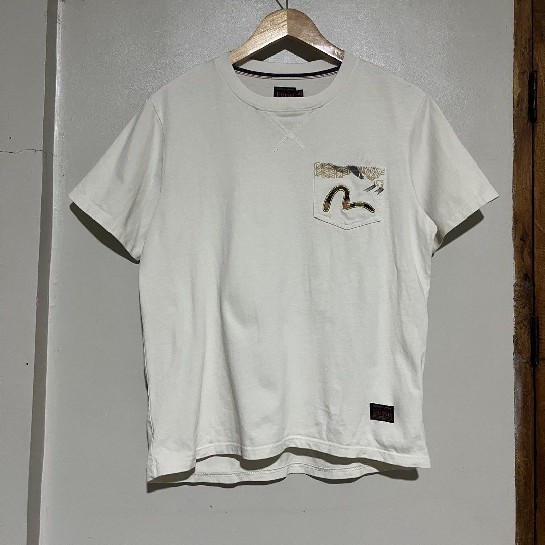 Evisu Heritage & Co White T-Shirt Size M (Category: Tshirts & Polo Shirts ) located in Argao. Submitted by secondcyclecollection (Listing ID 1470849222, Image 2). Description: - Brand: Evisu Heritage (Custom made) - Size: Medium - Color: Dirty White - Graphic print on back with gold wave details and lettering - Chest pocket with embroidered logo - Unique extra small pockets on the lower back - Ribbed collar with V-stitch inset - Clean condition t