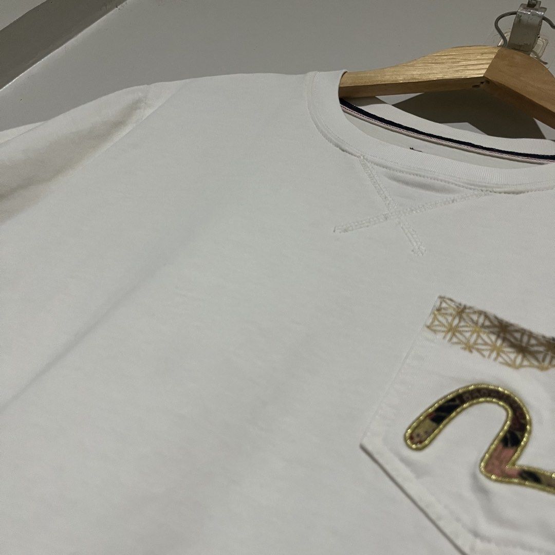 Evisu Heritage & Co White T-Shirt Size M (Category: Tshirts & Polo Shirts ) located in Argao. Submitted by secondcyclecollection (Listing ID 1470849222, Image 3). Description: - Brand: Evisu Heritage (Custom made) - Size: Medium - Color: Dirty White - Graphic print on back with gold wave details and lettering - Chest pocket with embroidered logo - Unique extra small pockets on the lower back - Ribbed collar with V-stitch inset - Clean condition t