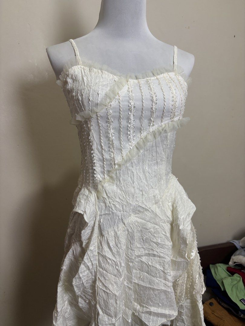 fairycore/Y2K-style camisole mini dress (Category: Dresses) located in Ajuy. Submitted by galitsabarat (Listing ID 1470793320, Image 2). Description: - Color: White - Style: Sleeveless with delicate spaghetti straps - Bodice: Structured corset style with a stylish diagonal ruffle trim - Fabric: Premium textured material throughout - Waistline: Trendy drop-waist design - Skirt: Layered, asymmetrical handkerchief hem - Closure: Secure back zipper -