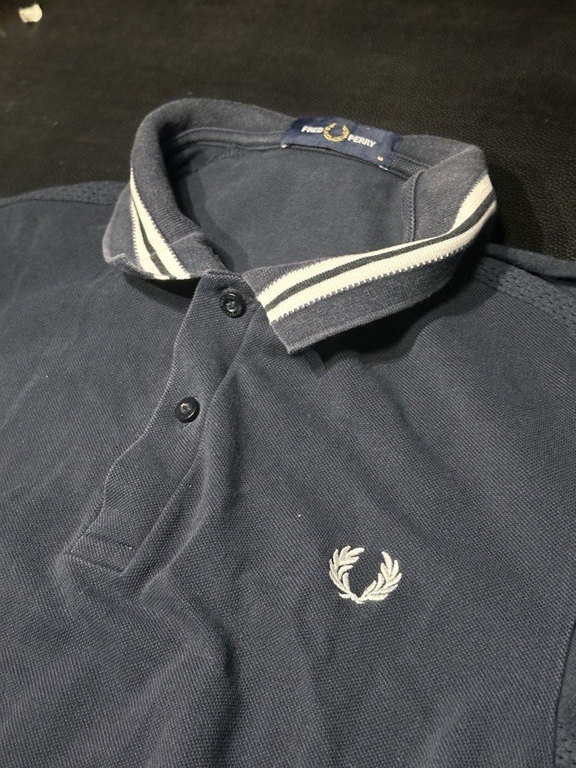 Fred Perry Navy Blue Polo Shirt Size M (Category: Tshirts & Polo Shirts ) located in Las Pinas. Submitted by boldbear_89ab40 (Listing ID 1470827052, Image 1). Description: - Brand: Fred Perry - Color: Dark Navy Blue - Size: Medium (tag on collar) - Details: Ribbed collar with white/dark stripes, iconic embroidered laurel wreath logo - Design: Breathable mesh patterned panels on shoulders and sleeves - Features: Short sleeves, front button placket