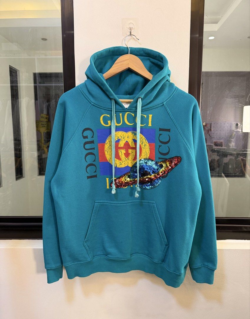 Gucci Graphic Pullover Hoodie (Category: Coats, Jackets and Outerwear) located in Paranaque City. Submitted by preluxeshop_ph (Listing ID 1470815131, Image 2). Description: Brand: Gucci •Style: Graphic Pullover Hoodie / Hooded Sweatshirt •Color: Turquoise / Teal Blue •Design Features: Vintage Gucci logo graphic print on the chest with a decorative sequin planet/appliqué detail, drawstring hood, and front kangaroo pocket •Made In: Italy •Condition