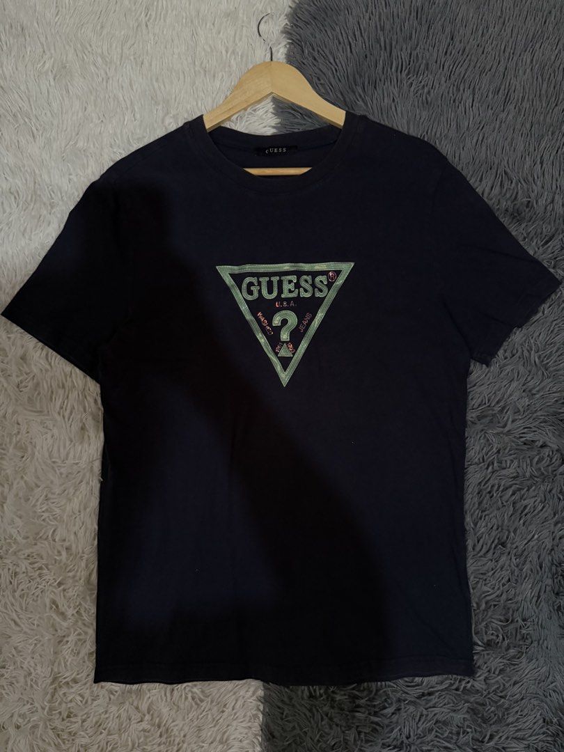 Guess Black T-Shirt with Triangle Logo (Category: Tshirts & Polo Shirts ) located in Manila. Submitted by keepercollection (Listing ID 1470832732, Image 1). Description: - Brand: Guess - Color: Dark navy blue - Design: Iconic green and red triangle logo on chest - Fit & Style: Regular fit, crew neck, short sleeves - Measurements: ~21 inches across chest, ~28 inches in length - Condition: Clean fabric, minimal signs of wear.