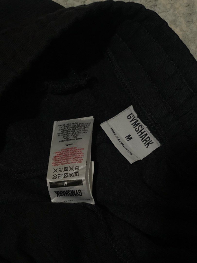 Gymshark Black Sweatpants Joggers Size M (Category: Joggers) located in Manila. Submitted by kuya_moto (Listing ID 1470827646, Image 3). Description: - Brand: Gymshark - Color: Black - Size: Medium - Material: 80% Cotton, 20% Polyester - Origin: Made in Bangladesh - Features: Soft fabric, elastic waistband with adjustable drawstring, embroidered white logo on the left leg, and ribbed ankle cuffs - Condition: Great for workouts or casual wear.