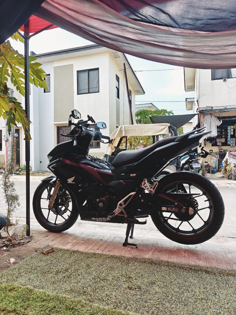Honda Matte Black Underbone Motorcycle (Category: Motorbikes for Sale) located in Manila. Submitted by risheejohn13344 (Listing ID 1470805919, Image 3). Description: Matte black finish with 'Black Series' decals on the front cowl. Custom handlebar grips, hand guards, and aftermarket mirrors installed. Gold-colored front fork suspension tubes. Clean body panels and alloy wheels. Parking stand down..