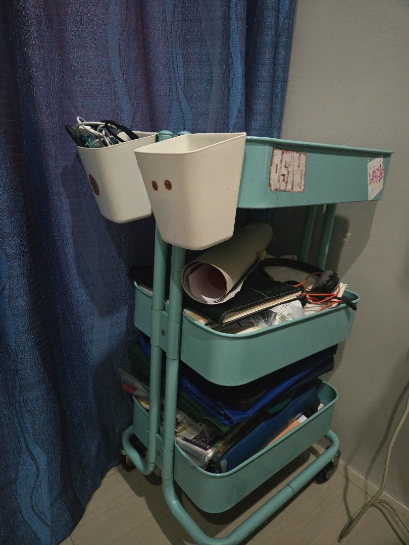 IKEA rolling utility cart with storage tiers (Category: Shelves, Cabinets & Racks) located in Pasig City. Submitted by izzy0202 (Listing ID 1470932079, Image 1). Description: - Color: Teal - Material: Metal with rolling wheels for easy mobility - Storage: 3 spacious tiers for books, notebooks, and clutter - Condition: Used with some stickers and daily use marks - Best for: Room, office, or kitchen organization.
