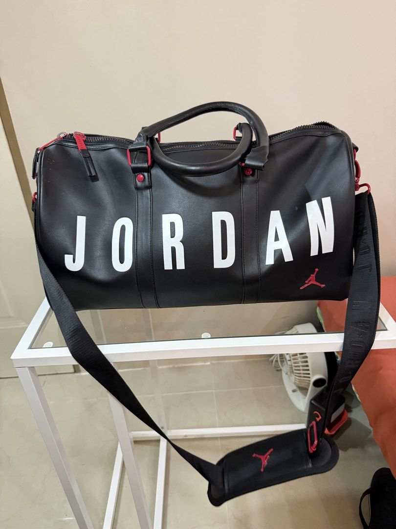 Jordan Black Duffle Bag with Red Accents (Category: Sling Bags) located in Rosario. Submitted by chippycoco (Listing ID 1470765902, Image 2). Description: - Color: Classic Black with bold White Jordan lettering - Accents: Signature Red Jumpman logo on front and shoulder strap pad - Hardware: Premium red hardware with matching Jordan-branded zipper pulls - Straps: Sturdy double carrying handles and an adjustable black shoulder strap - Condition: B