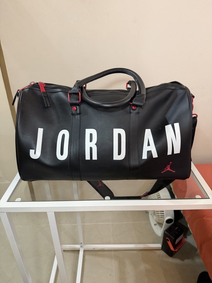 Jordan Black Duffle Bag with Red Accents (Category: Sling Bags) located in Rosario. Submitted by chippycoco (Listing ID 1470765902, Image 1). Description: - Color: Classic Black with bold White Jordan lettering - Accents: Signature Red Jumpman logo on front and shoulder strap pad - Hardware: Premium red hardware with matching Jordan-branded zipper pulls - Straps: Sturdy double carrying handles and an adjustable black shoulder strap - Condition: B