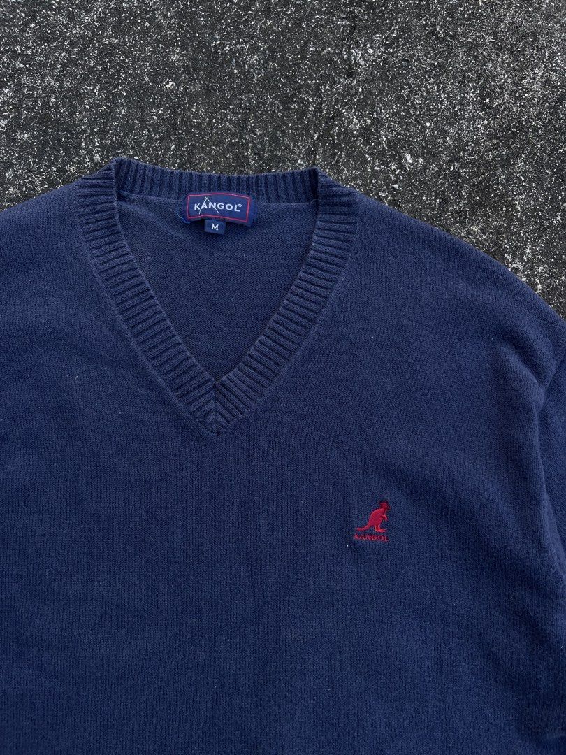 Kangol Navy Blue V-Neck Knit Sweater Size M (Category: Coats, Jackets and Outerwear) located in Tarlac. Submitted by supremo.0 (Listing ID 1470747149, Image 2). Description: - Brand: Vintage Knitted Kangol - Color: Navy blue - Size: Medium (tag on collar) (21x26) - Style: V-neck sweater with ribbed collar, cuffs, and hem - Details: Red embroidered kangaroo logo on left chest, small blue woven label near bottom hem - Authenticity: Interior license