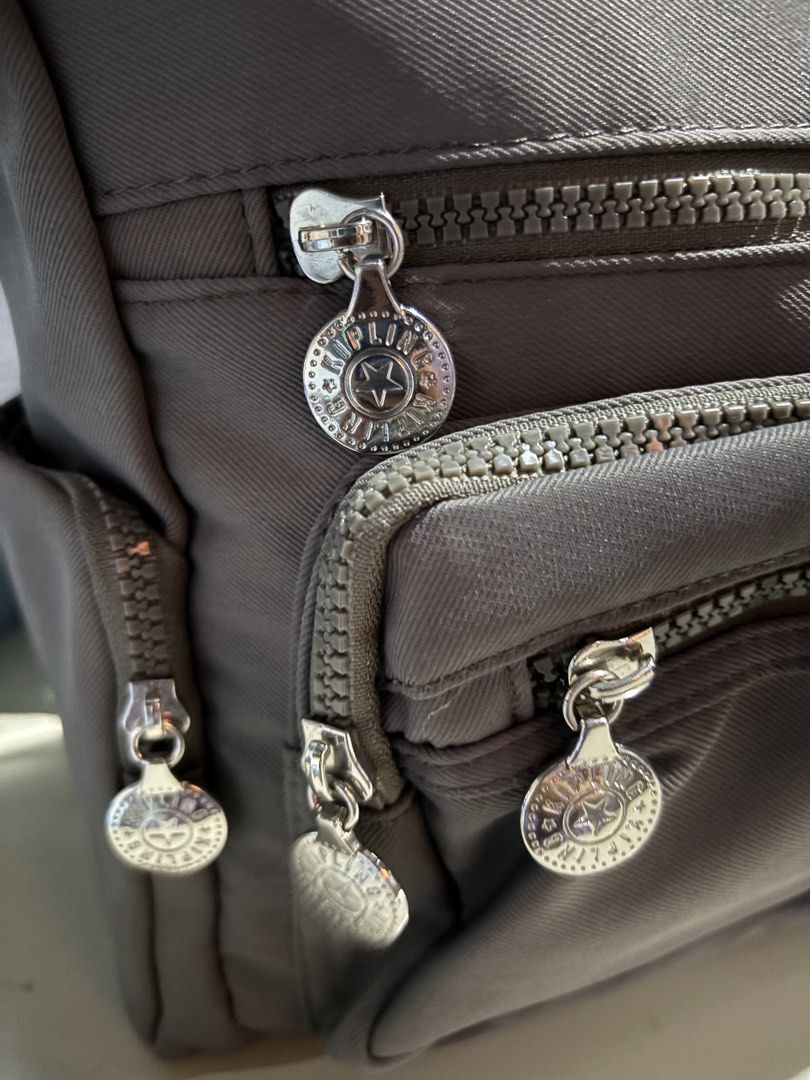 Kipling Grey Crossbody Bag with Multiple Zipper Pockets (Category: Cross-body Bags) located in Rizal. Submitted by va_nes_sa_ (Listing ID 1470818428, Image 2). Description: - Color: Grey - Material: Durable nylon - Strap: Adjustable with metal buckle detail - Pockets: Multiple front zip compartments, back exterior zip pocket, and inner storage pockets - Design: Pleated front panel with round metallic zipper pulls and logo badge - Condition: Clean