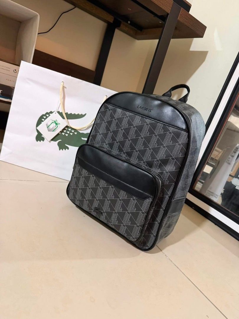 Lacoste Monogram Backpack Black Grey (Category: Backpacks) located in Caloocan City. Submitted by luckyocean_e40f38 (Listing ID 1470822610, Image 1). Description: Lacoste backpack in black and grey monogram pattern. Smooth black leather accents on the top and front zip pocket. Silver debossed Lacoste branding near the top. Padded top handle and adjustable straps. Matching Lacoste paper bag included in the background. Clean structure, ready for da