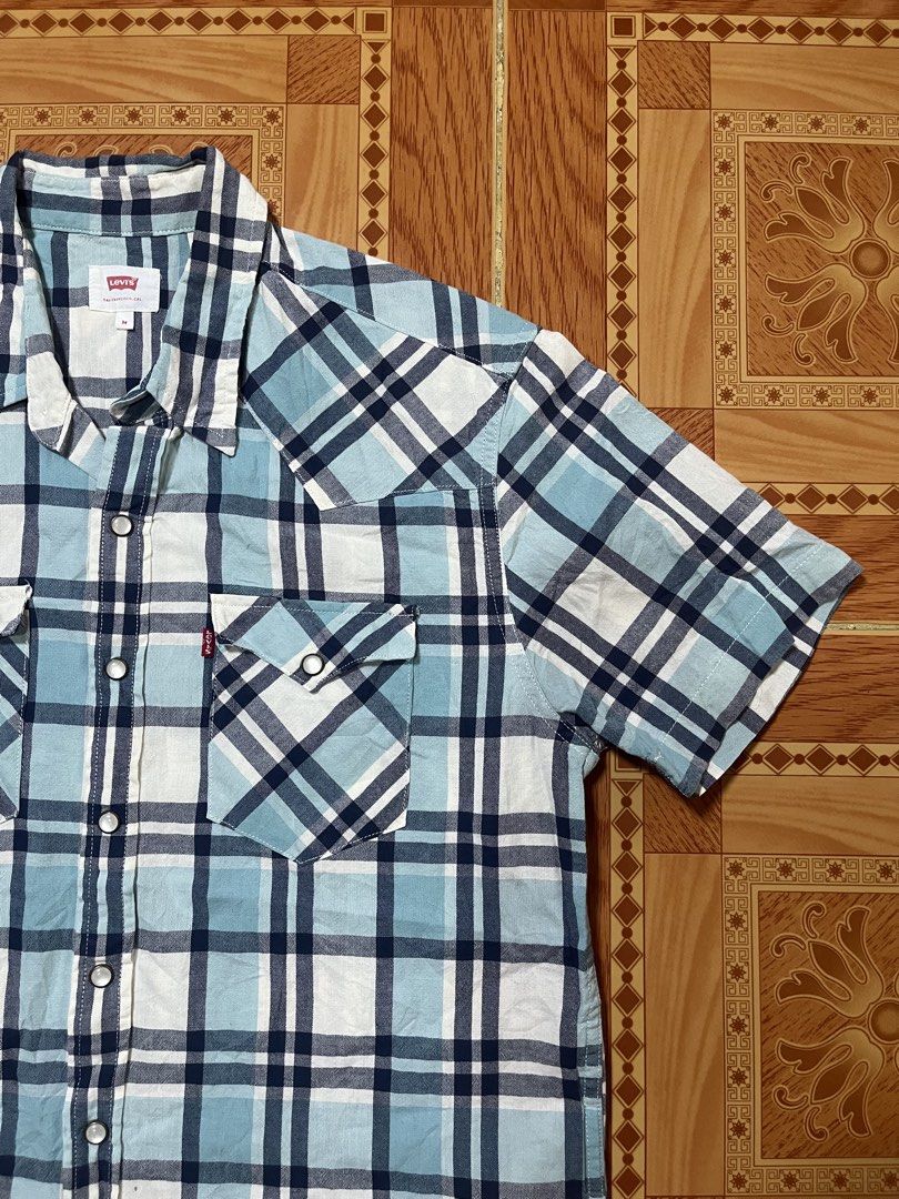 Levi's Blue Plaid Short Sleeve Button-Up Shirt (Category: Activewear) located in Kidapawan. Submitted by azythrift (Listing ID 1470824329, Image 2). Description: - Brand: Levi's - Style: Short sleeve button-up shirt - Pattern: Blue, white, and navy plaid - Details: Pearl snap front closure, two chest pockets with snaps, iconic Levi's red tab - Size: Medium.