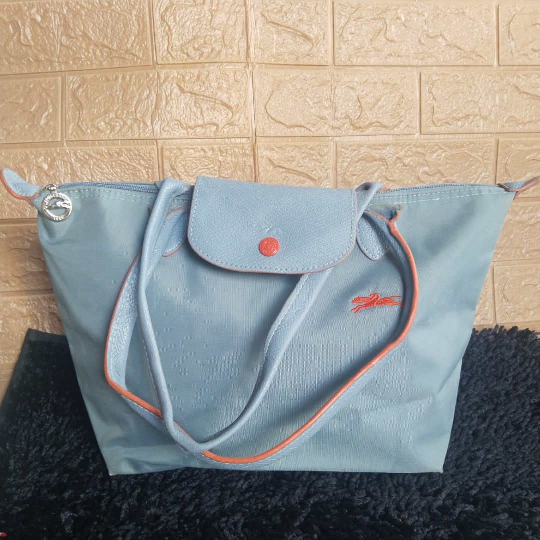 Longchamp Le Pliage Blue Tote Bag (Category: Luxury Bags & Wallets) located in Lubao. Submitted by dione_closet503 (Listing ID 1470932067, Image 1). Description: - Authentic Longchamp nylon tote in light blue - Features leather handles, flap closure, and iconic red embroidered horse logo - Silver-tone zipper pull with detailed jockey engraving - Classic foldable design with a spacious interior for daily essentials - Condition: Good, with some min