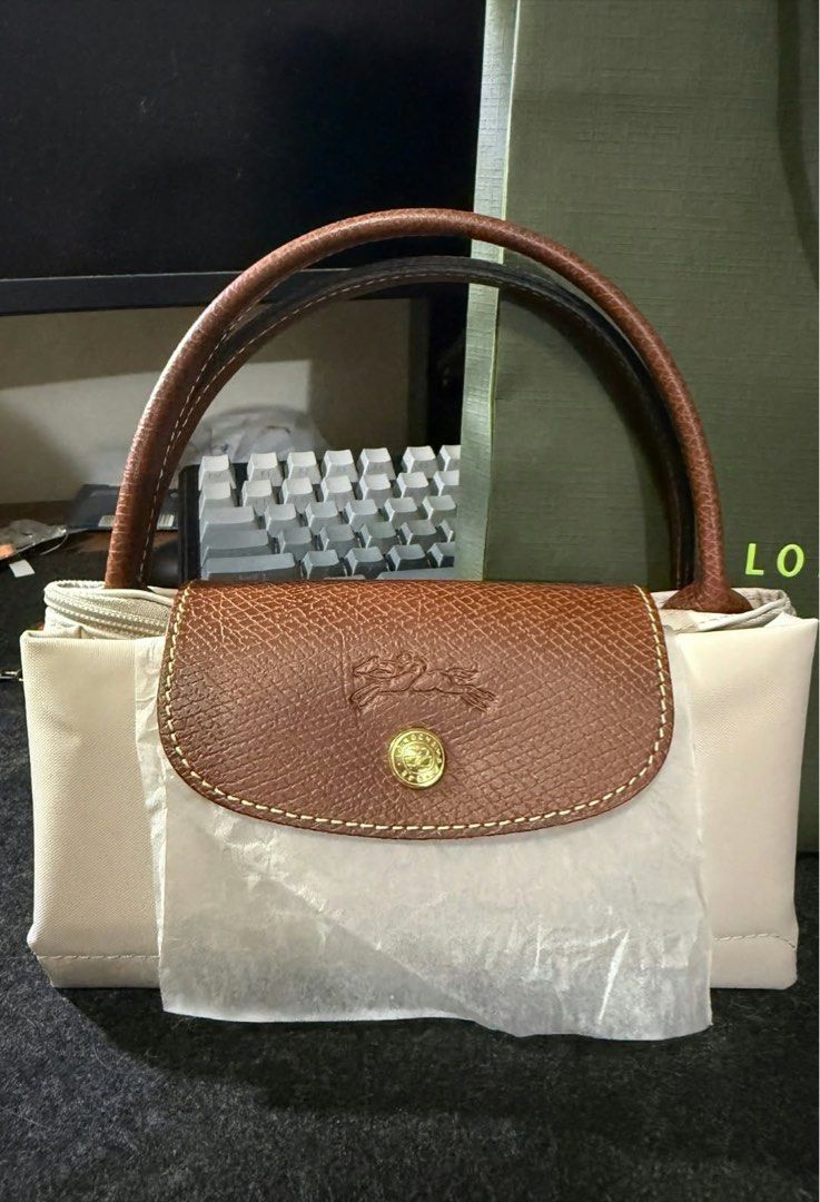Longchamp Le Pliage Handbag Beige Brown (Category: Luxury Bags & Wallets) located in Manila. Submitted by 123cheesedog (Listing ID 1470757793, Image 3). Description: - Brand: Longchamp Le Pliage Bought from RUSTANS - Condition: Brand new, unused, and still wrapped in protective paper - Color: Elegant beige nylon body with rich brown leather handle and flap - Hardware: Classic gold-tone hardware with signature horse logo zipper pull - Style: Timel