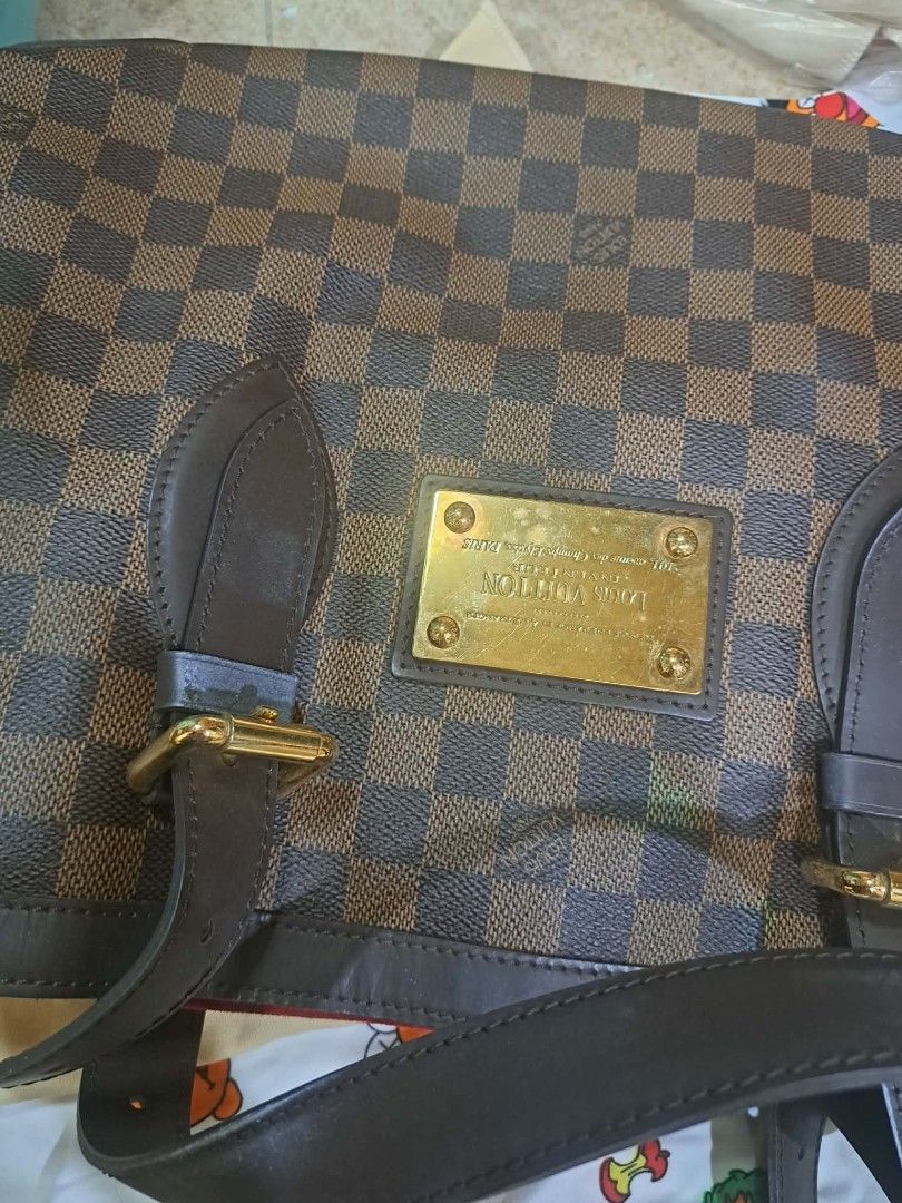 Louis Vuitton Hampstead MM Damier Ebene (Category: Luxury Bags & Wallets) located in Bacolod City. Submitted by legitseller2024 (Listing ID 1470886431, Image 3). Description: Louis Vuitton Hampstead MM tote bag in Damier Ebene canvas. Classic brown check pattern with dark brown leather trim and gold-tone hardware plaque on the front. Double shoulder straps with buckle adjustments. Includes the original dust bag. Hardware shows some surface scratc