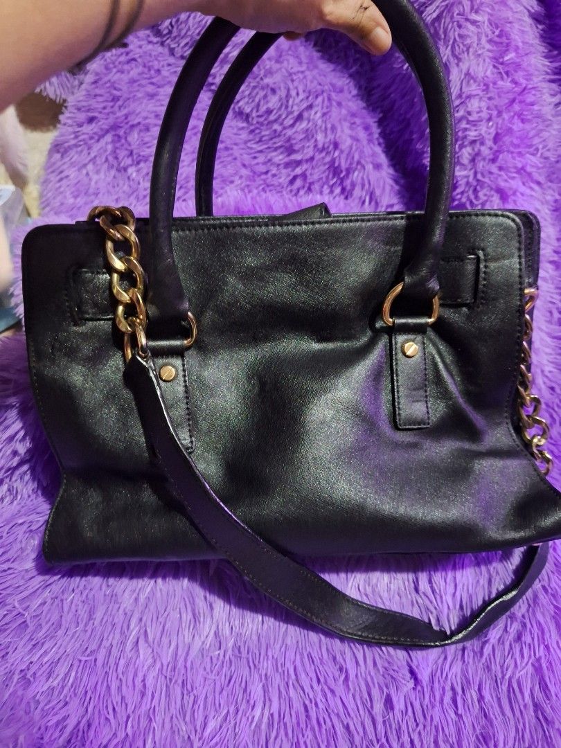 Michael Kors Black Hamilton Handbag With Gold Hardware (Category: Luxury Bags & Wallets) located in Quezon City. Submitted by cloudymay (Listing ID 1470820362, Image 3). Description: Black Michael Kors satchel bag. Gold lock detail on the front, plus a chunky gold chain strap on the side. Double top handles. Tan fabric lining inside with zipper pockets. Structured shape with pebbled texture. Zip closure on top. Min signs of wear on leather: folds