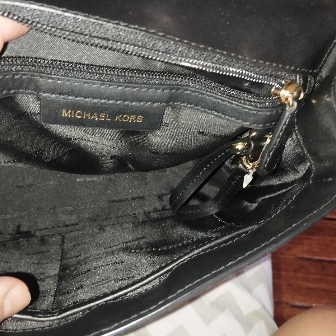 Michael Kors Black Leather Handbag with Gold Hardware (Category: Cross-body Bags) located in Manila. Submitted by lene48 (Listing ID 1470853295, Image 3). Description: Black leather Michael Kors handbag with prominent gold MK logo on the front flap. Structured top handle design paired with a chain-accented shoulder strap. Interior lined in black branded fabric featuring zippered pockets and a slip pocket. Gold tone protective feet on the base. Mi