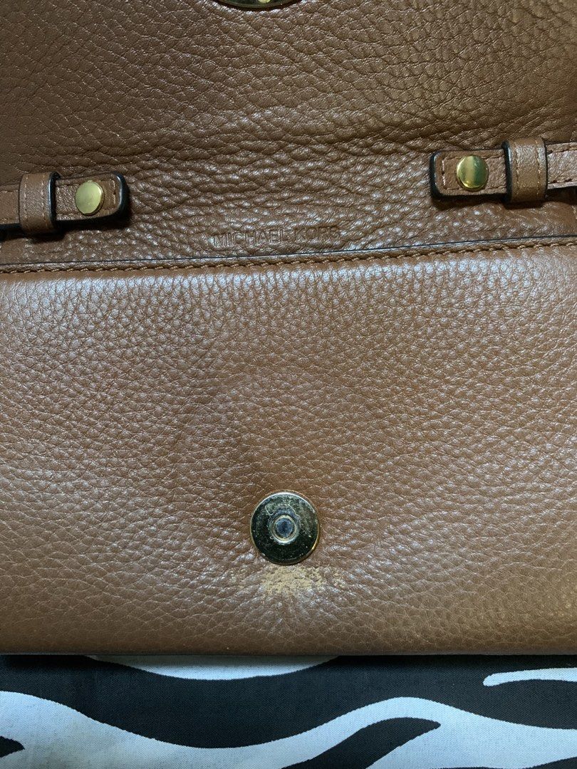 Michael Kors Brown Leather Crossbody Bag (Category: Cross-body Bags) located in Manila. Submitted by usagichan_rabbit (Listing ID 1470744928, Image 3). Description: - Brand: Michael Kors - Material: Brown pebbled leather with gold-tone hardware - Design: Crossbody bag featuring a front flap with a large round MK logo emblem and chic chain strap accents - Interior: Multiple compartments, card slots, and clean fabric lining - Strap: Adjustable leat