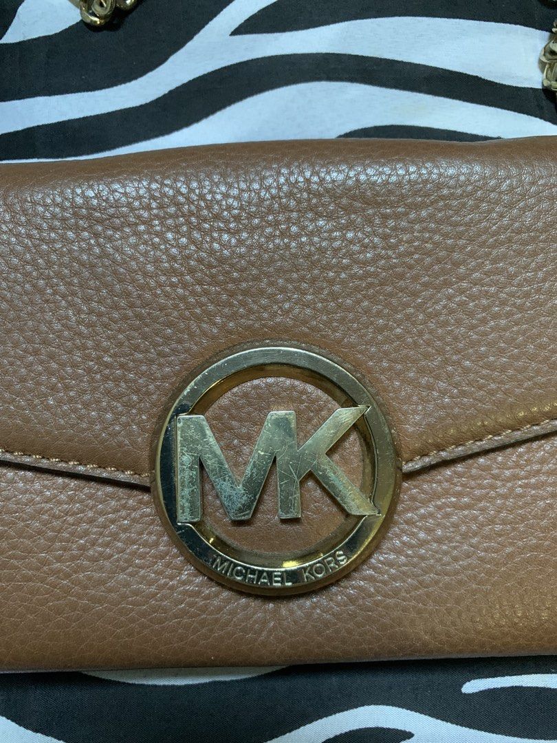 Michael Kors Brown Leather Crossbody Bag (Category: Cross-body Bags) located in Manila. Submitted by usagichan_rabbit (Listing ID 1470744928, Image 2). Description: - Brand: Michael Kors - Material: Brown pebbled leather with gold-tone hardware - Design: Crossbody bag featuring a front flap with a large round MK logo emblem and chic chain strap accents - Interior: Multiple compartments, card slots, and clean fabric lining - Strap: Adjustable leat