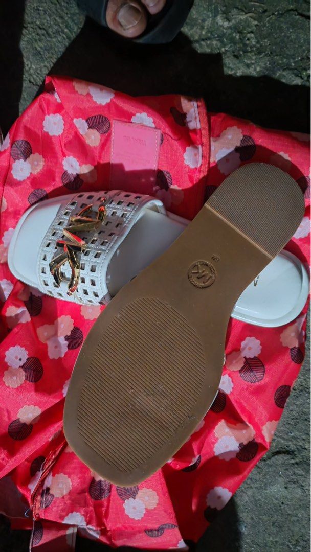 Michael Kors White Sandals Size 6M (Category: Flats & Sandals) located in Baguio. Submitted by markmartin3 (Listing ID 1470886215, Image 2). Description: - Brand: Michael Kors - Style: White slip-on sandals / flat style - Size: 6M - Details: Cutout grid strap design with signature gold-tone logo hardware - Soles: White inner sole with stamped branding, brown outer sole with textured grip and embossed MK logo circle - Condition: Clean finish, perf