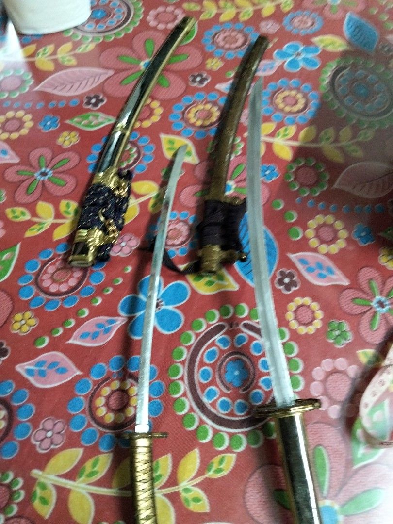 Miniature Katana Sword Set with Scabbards (Category: Vintage Collectibles) located in Abucay. Submitted by cristineca20489 (Listing ID 1470914802, Image 2). Description: - Set of 2 miniature katana display swords - Features intricate gold-tone details on handles and sheaths - Scabbards wrapped in black cord and purple/gold cord - Perfect for desk setups and collections - Note: Display pieces only with minor wear on metal finishes -46cm and 36cm.