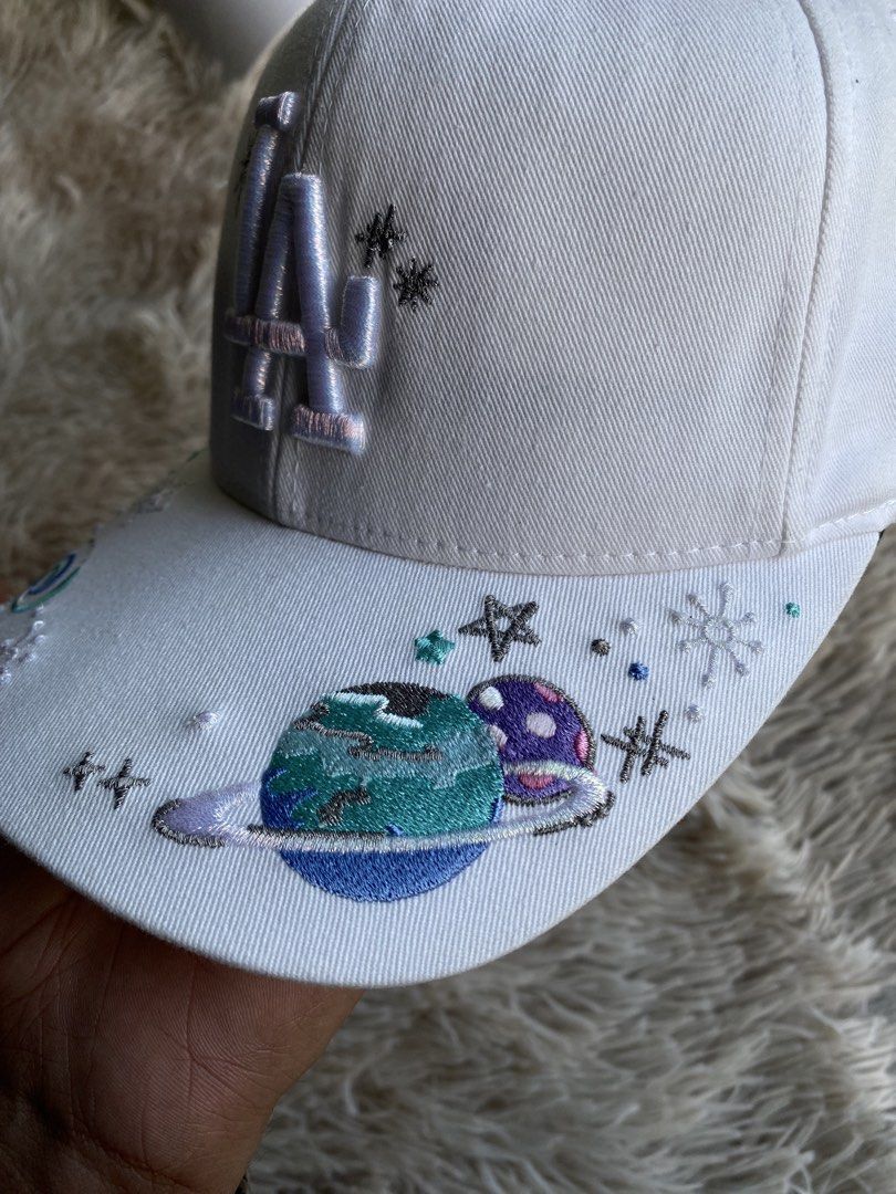 MLB LA Dodgers “Galaxy / Cosmic Custom Art” Cap (White) 🧢✨ (Category: Caps & Hats) located in Puerto Princesa. Submitted by thriftedheatshub (Listing ID 1470859788, Image 3). Description: 💰 Price: ₱679 + Shipping Fee🏷️ (Steal price) Condition: Good as New Condition (9.8/10 — pristine white crown & visor, heavy 3D embroidered “LA” logo with metallic silver thread accents, vibrant galaxy/planet/constellation embroidered custom art across brim) �