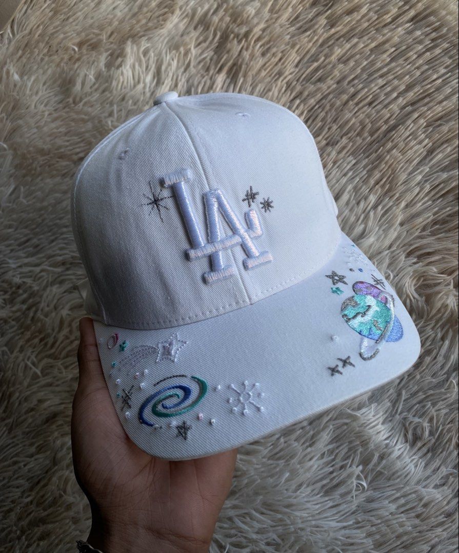 MLB LA Dodgers “Galaxy / Cosmic Custom Art” Cap (White) 🧢✨ (Category: Caps & Hats) located in Puerto Princesa. Submitted by thriftedheatshub (Listing ID 1470859788, Image 1). Description: 💰 Price: ₱679 + Shipping Fee🏷️ (Steal price) Condition: Good as New Condition (9.8/10 — pristine white crown & visor, heavy 3D embroidered “LA” logo with metallic silver thread accents, vibrant galaxy/planet/constellation embroidered custom art across brim) �