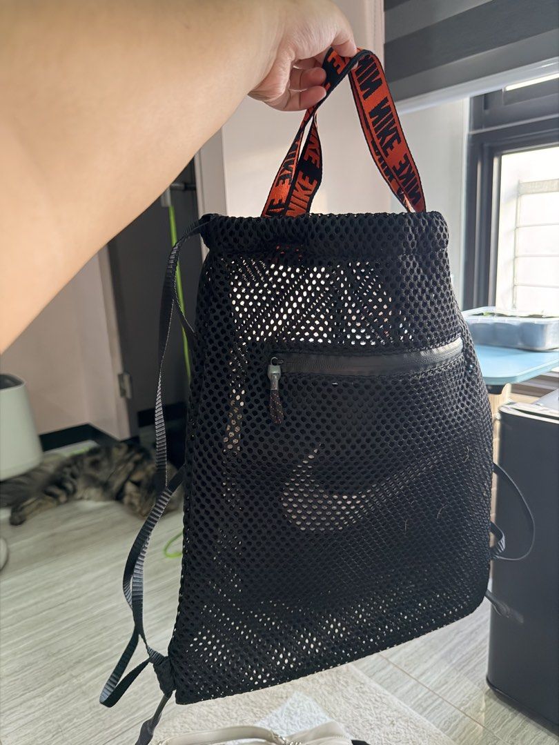Nike Mesh Drawstring Backpack Black Orange Straps (Category: Backpacks) located in Quezon City. Submitted by minimalistsmercurymanila (Listing ID 1470869999, Image 1). Description: - Brand: Nike - Type: Mesh Drawstring Backpack - Color: Black with bright orange accents - Features: Repeating Nike lettering on top grab handles, front zippered pocket with dark pull tab - Material: Lightweight and breathable mesh - Straps: Thin black shoulder strap s