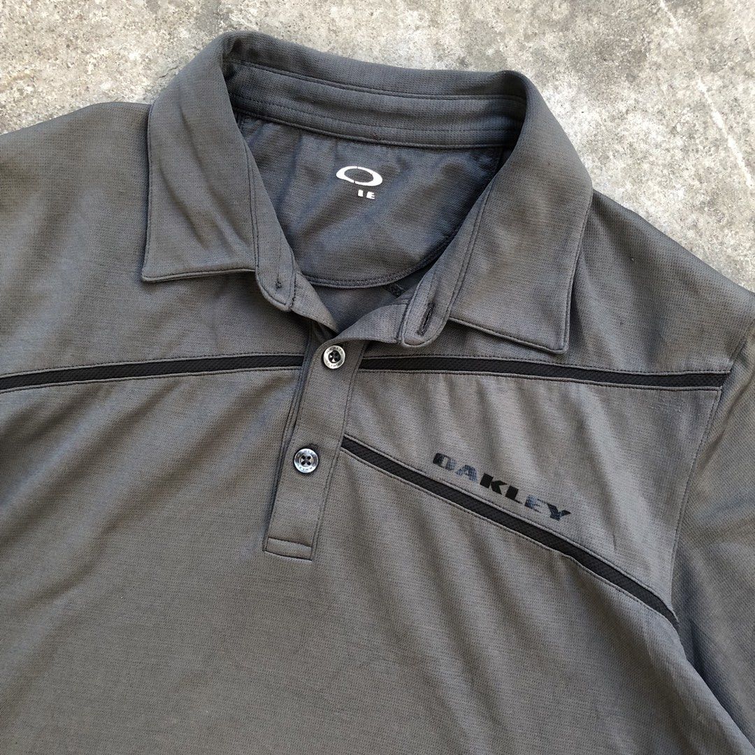 Oakley Golf Polo Shirt Grey (Category: Tshirts & Polo Shirts ) located in Manila. Submitted by threezzz (Listing ID 1470834868, Image 1). Description: - Brand: Oakley - Color: Grey with contrasting dark chest stripes - Material: Breathable textured fabric - Design: Short sleeves, standard collar, two-button placket with branded buttons - Branding: Oakley logo printed on left chest and back shoulder - Style: Casual sportswear / golf polo.
