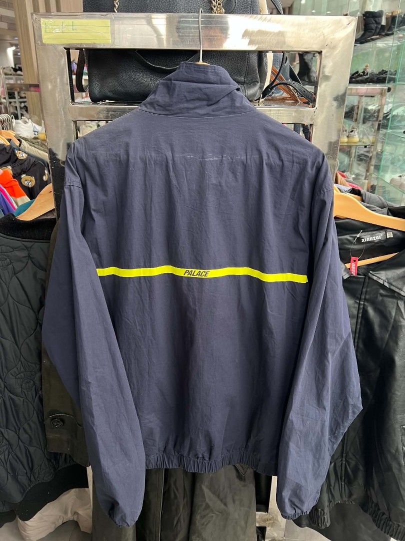 Palace Navy Windbreaker Jacket with Yellow Stripe (Category: Coats, Jackets and Outerwear) located in Urdaneta. Submitted by jayceegarage (Listing ID 1470881057, Image 2). Description: - Brand: Palace - Color: Dark blue with a bold yellow chest stripe - Closure: Full zip front with silver zipper pull - Features: Elastic cuffs and hem, white Palace collar label - Material: Lightweight and comfortable - Condition: Great throw-on piece for cooler da