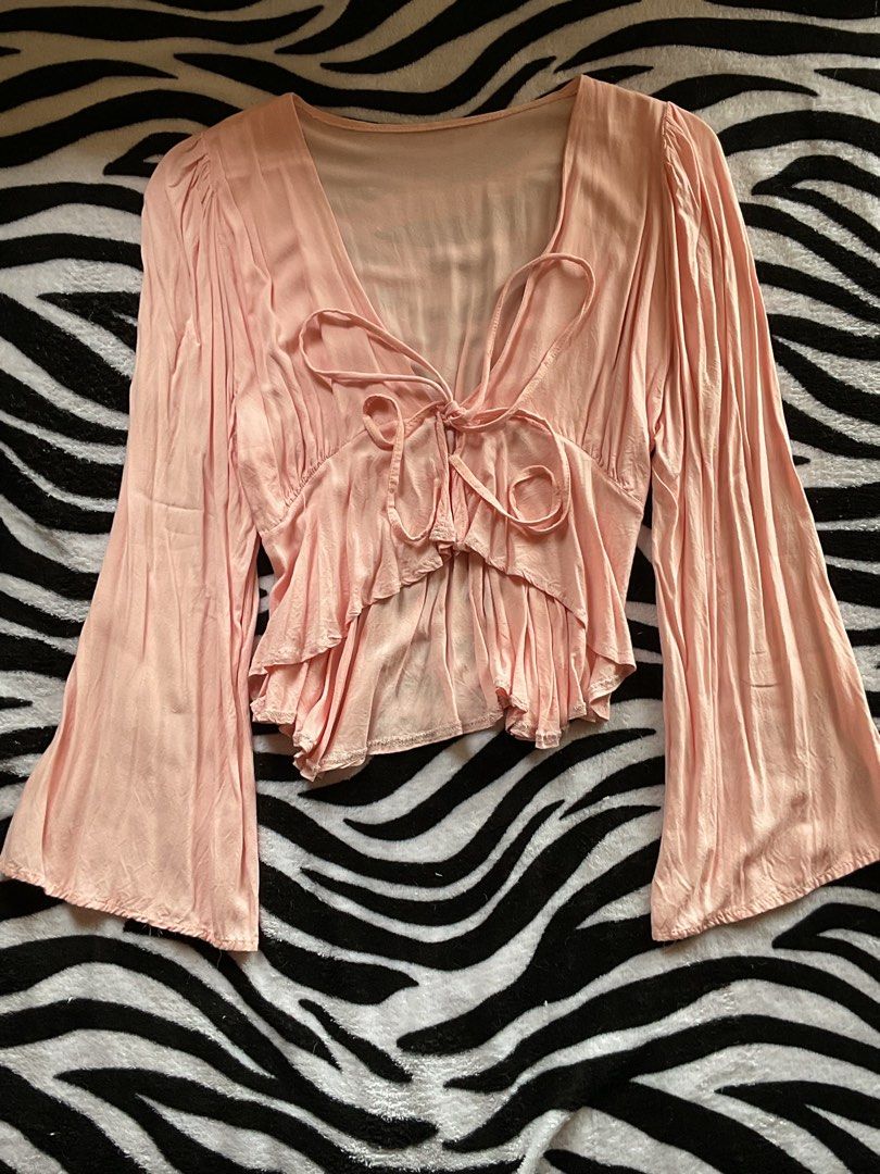 Pink Tie Front Bell Sleeve Top (Category: Blouses) located in Baguio. Submitted by prelovedbymb_11 (Listing ID 1470871293, Image 1). Description: - Color: Light pink - Design: V-neck with front tie closures - Sleeves: Long flared bell sleeves - Hem: Layered ruffled hem - Material: Lightweight and soft-draped fabric - Style: Casual, chic, and great for hanging out with friends.