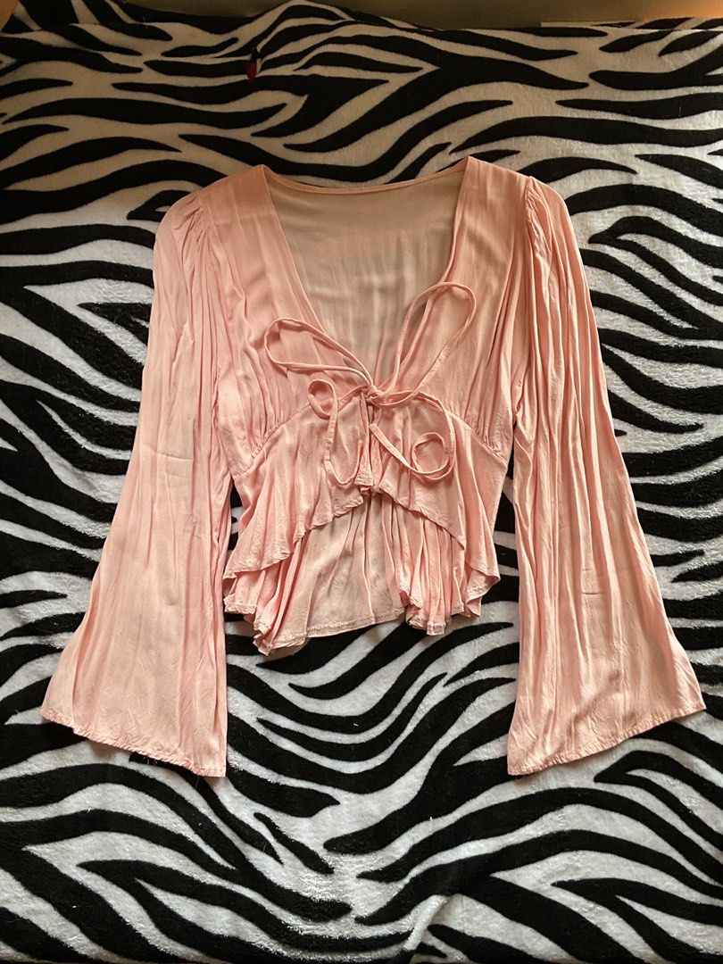 Pink Tie Front Bell Sleeve Top (Category: Blouses) located in Baguio. Submitted by prelovedbymb_11 (Listing ID 1470871293, Image 2). Description: - Color: Light pink - Design: V-neck with front tie closures - Sleeves: Long flared bell sleeves - Hem: Layered ruffled hem - Material: Lightweight and soft-draped fabric - Style: Casual, chic, and great for hanging out with friends.