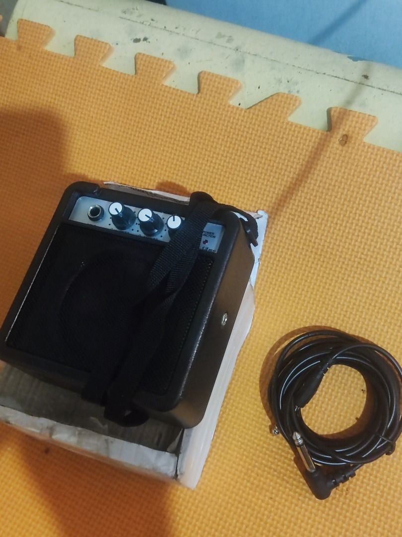 Portable Mini Amplifier with Strap and Battery (Category: Soundbars, Speakers & Amplifiers) located in Valenzuela. Submitted by reynoldyabut6536 (Listing ID 1470768114, Image 2). Description: Black portable mini amplifier 5watts unit with a carrying strap attached. Operates on a 9V SEPE battery, which is included inside the battery compartment. Open battery cover shown next to the slot. Plastic casing with vent grilles. Comes with a white cardboa